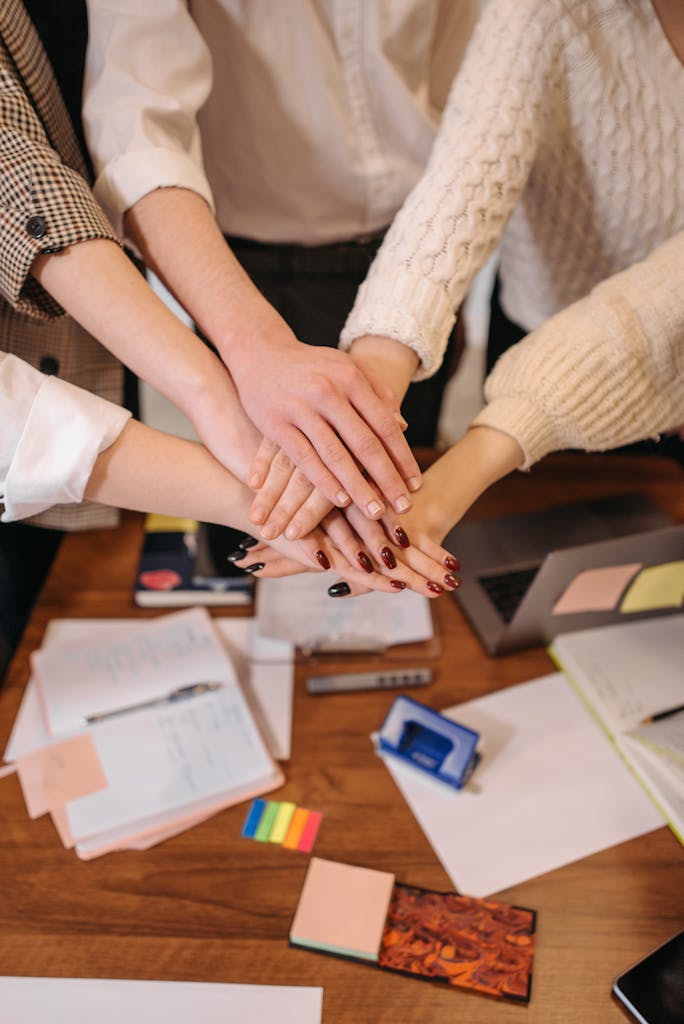 A top-down view of hands stacked together over an office table, symbolizing teamwork.