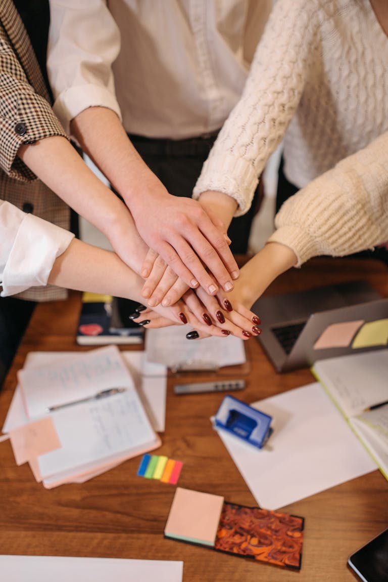 Team Building Program Example – Building Trust 1 A top-down view of hands stacked together over an office table, symbolizing teamwork.