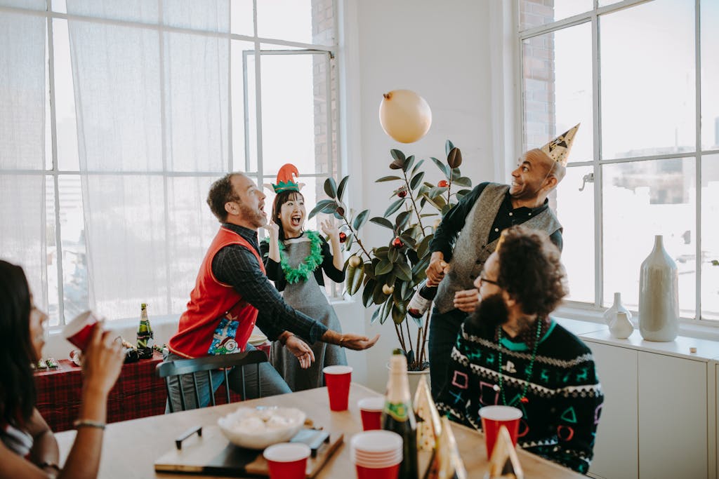 Cheerful office holiday party with adults in festive Christmas sweaters celebrating with food and drinks.