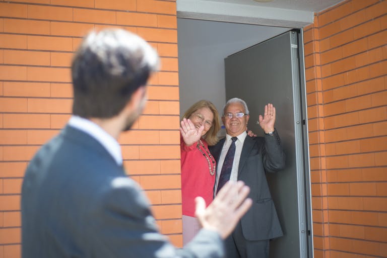 How to Say Farewell to a Coworker: Simple Ways to Say Goodbye, Thank You, and Good Luck 1 Smiling couple waving goodbye from home entrance with real estate agent in foreground.